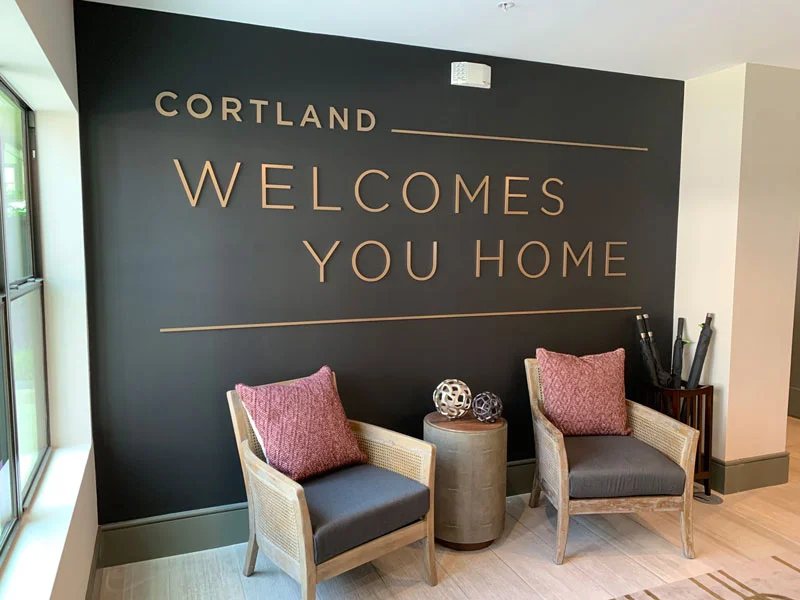 Image of a lobby seating area with two chairs and a small table. The phrase "Cortland welcomes you home" is on the wall.